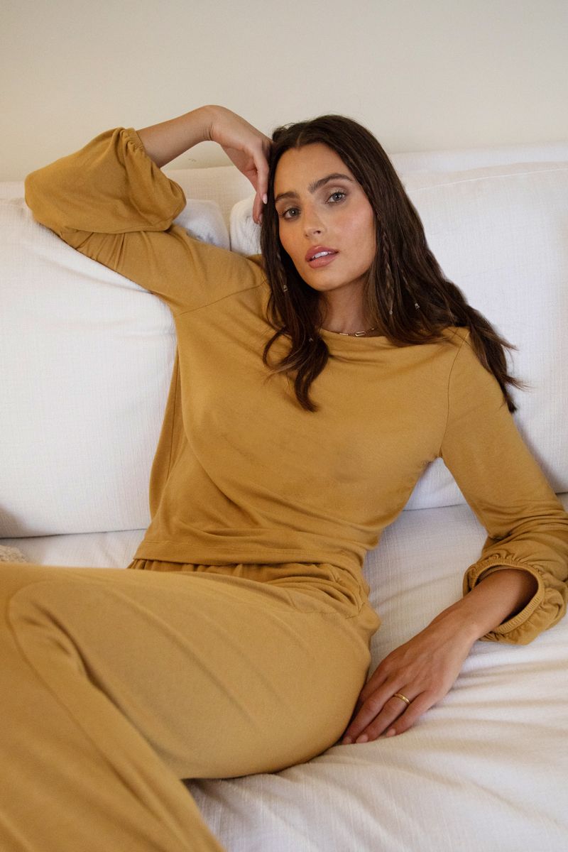 model sitting back on the couch in camel colored matching lounge set of pants and long sleeve